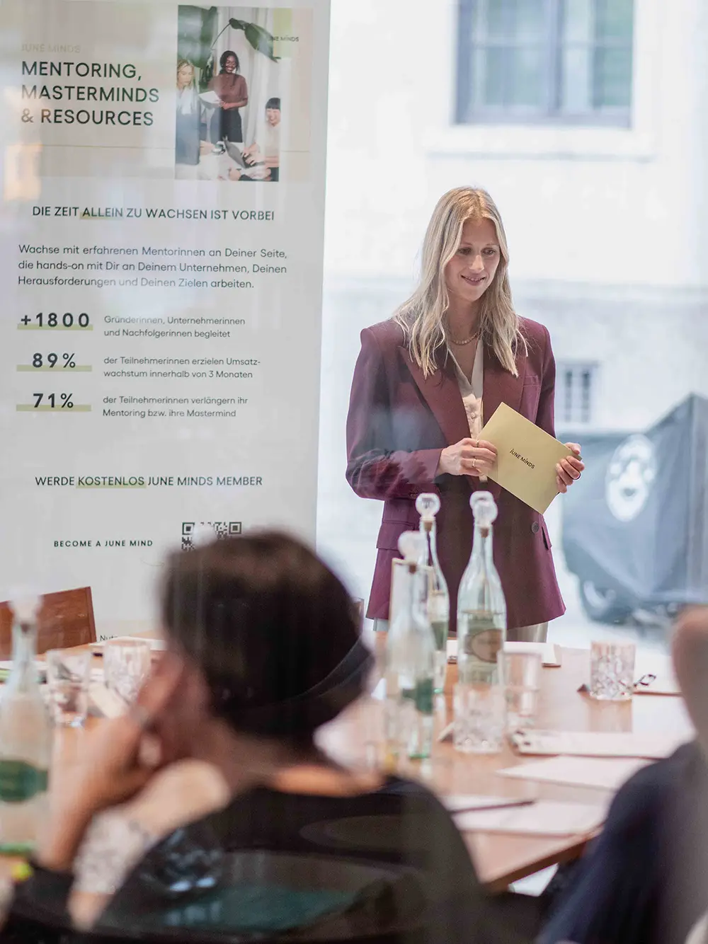 Magdalena spricht mit Unterlagen in der Hand vor Teilnehmenden während eines Business-Workshops
