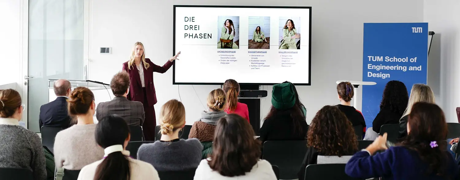 Magdalena hält einen Vortrag vor Publikum und präsentiert Inhalte auf einem Bildschirm