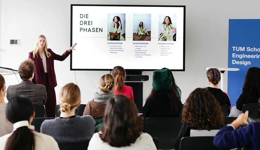 Magdalena hält einen Vortrag vor Publikum und präsentiert Inhalte auf einem Bildschirm